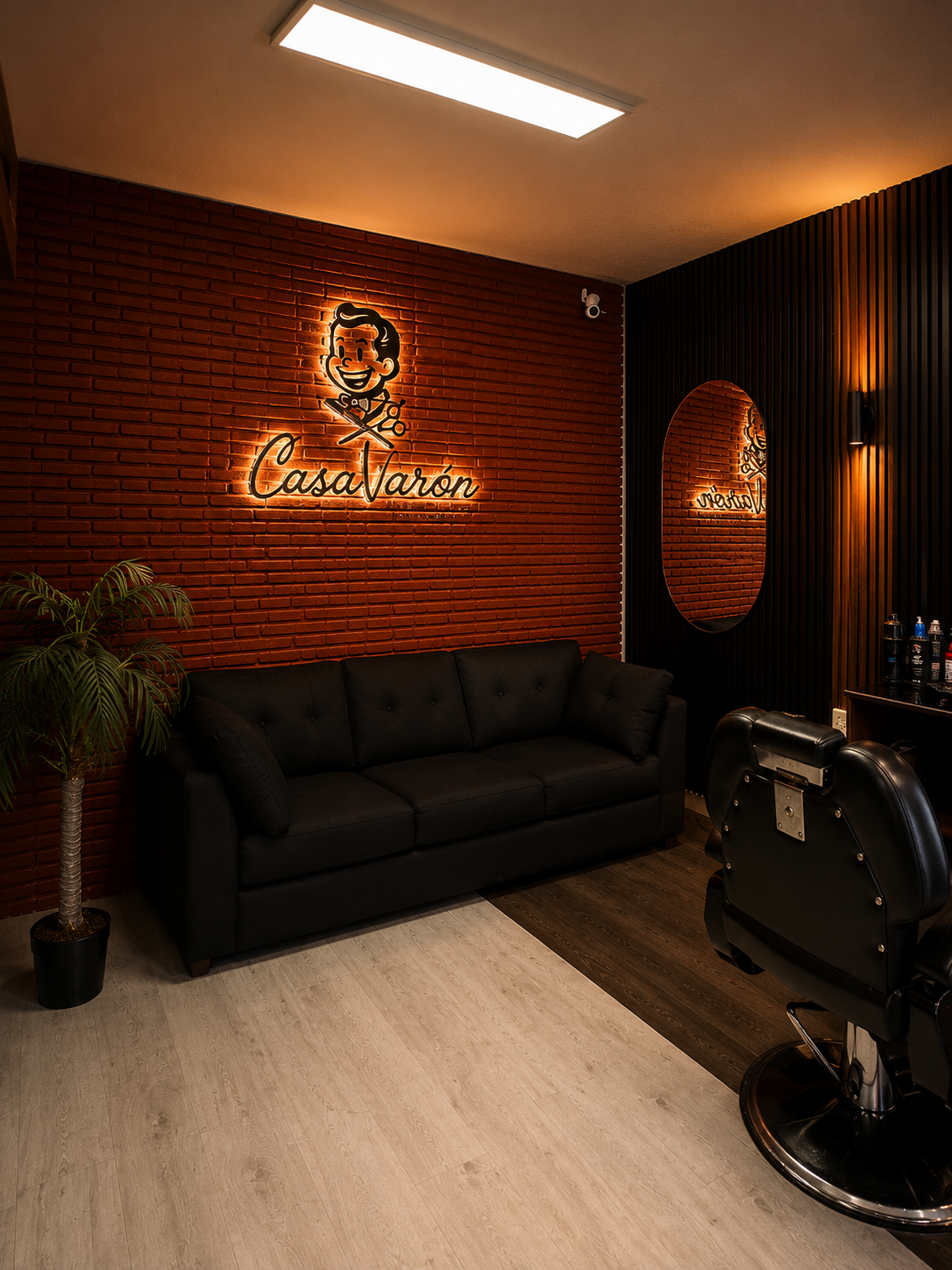 Interior de Casa Varón: pared de ladrillo rojo con el logotipo de la mascota en neón ámbar, sofá negro y silla de barbero.